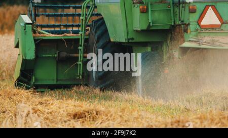 Back-view of a modern green combine working on the field. Forest and ...