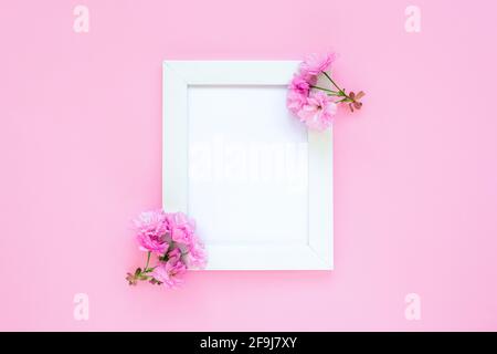 Blank picture frame and cherry blossom on pink background. Copy space for text. Top view, flat lay. Stock Photo