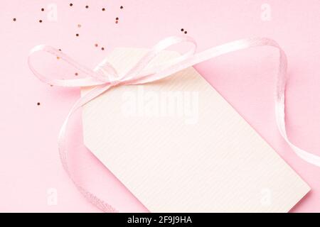 Blank price tag with pink ribbon bow on pink background with confetti. Stock Photo