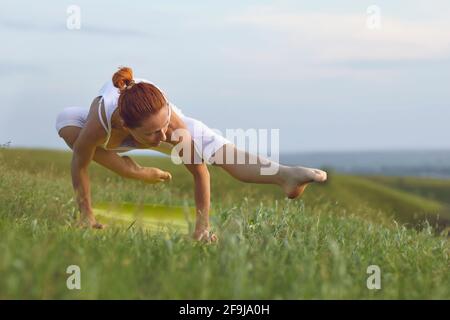 Motivated yoga lover balancing on hands practicing asanas in peaceful summer field Stock Photo