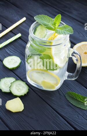 Sassy  water  slimming or infused water with lemon, cucumber and ginger in the glass on the black wooden  background. Location vertical. Stock Photo