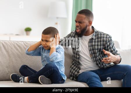 Aggressive Black Father Shouting At Unhappy Kid Boy At Home Stock Photo