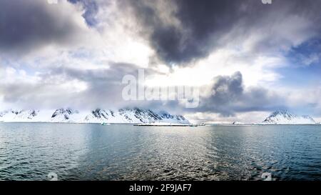 Panorama of snow covered mountains with low cloud. Golden sunlight at dusk. Svalbard, a Norwegian archipelago between mainland Norway and the North Po Stock Photo