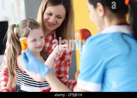 Doctor holding jar of medicine and apple in front of little girl and mother Stock Photo