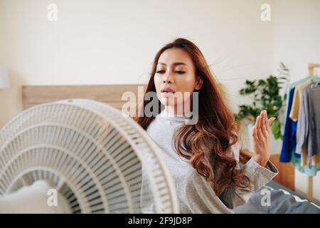 Young woman standing in front of fan enjoying fresh air on hot day Stock Photo