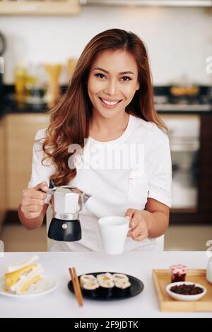 Portrait of positive young Asian woman having breakfast and cup of coffee at home Stock Photo