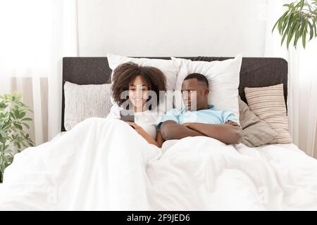 Man having problem while girlfriend using smartphone in bed Stock Photo