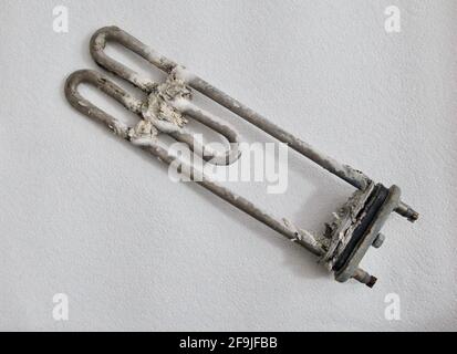 Charred and scaled heating element from washing machine on white background Stock Photo