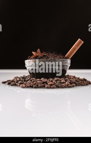Natural homemade body coffee scrub on coffee beans on a white table with reflection. Handmade spa cosmetic. Salt scrub with ground coffee cinnamon and cloves. Vertical photo. Stock Photo