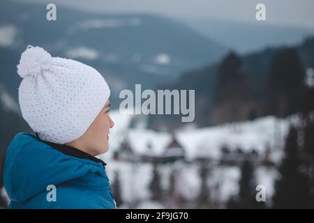 Candid portrait of boy with childish joyful smile in winter white hat and blue jacket. Real portrait of natural smiling teenager in winter months. No Stock Photo