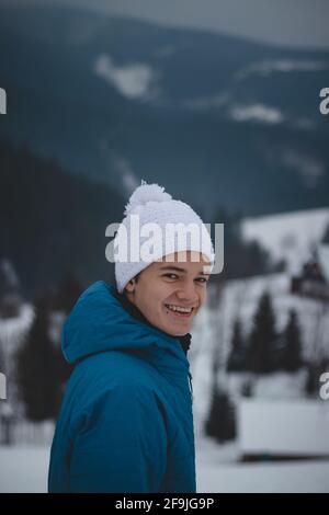 Candid portrait of a boy with childish joyful smile in a winter white hat and blue jacket. Real portrait of a natural smiling teenager in winter month Stock Photo