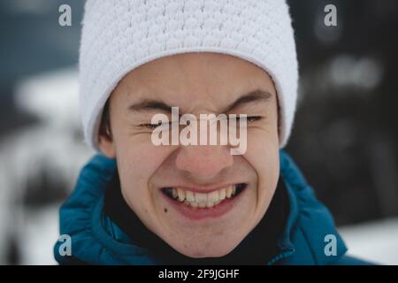 Candid portrait of a boy with a childish joyful smile in a winter white hat and blue jacket. Real portrait of a natural smiling teenager in the winter Stock Photo