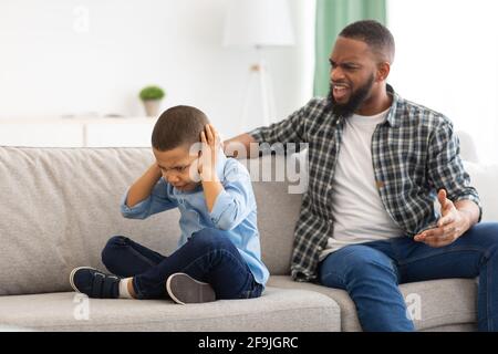 Angry Black Dad Shouting At Unhappy Son Sitting At Home Stock Photo