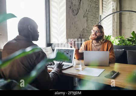 Two contemporary businessmen discussing project during meeting at cafe table and using laptops, copy space Stock Photo