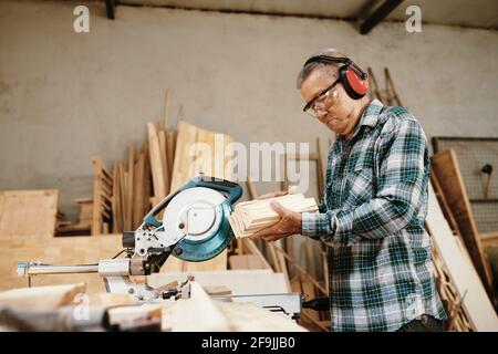 Experienced senior Vietnamese carpenter looking at wooden blocks he cut with circula saw Stock Photo