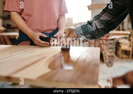 Senior carpenter showing apprentice how to apply oil on sanded wood board Stock Photo