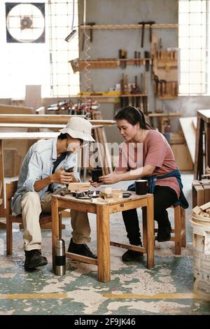 Young Asian carpenters having coffee break and discussing refence picture that customer sent via social media Stock Photo