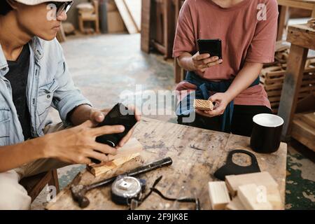 Carpenter phototgraphing wooden blocks for social media when having short coffee break in workshop Stock Photo