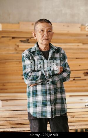 Portrait of serious senior Vietnamese carpenter in plaid shirt crossing arms and looking at camera Stock Photo