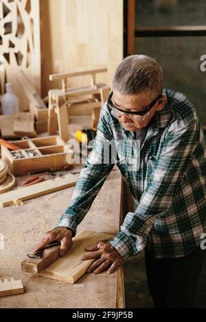 Senior man in goggles working with wooden blocks at workbench Stock Photo