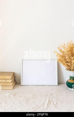 Home decor mock-up, blank picture frame near white painted concrete wall ,vase with dried yellow oat stalks, old books Stock Photo