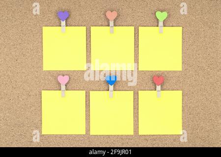 Six yellow stickers with multicolored clothespins on a cork board. Stock Photo
