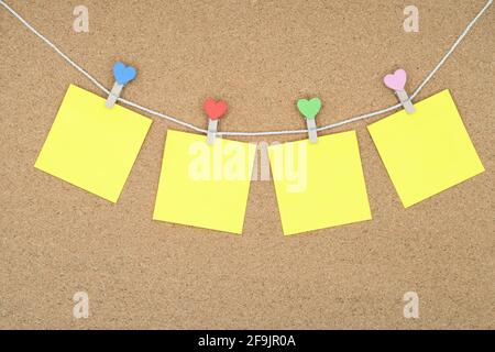 Four yellow stickers on a rope with multi-colored clothespins. Stickers on the cork board. Stock Photo