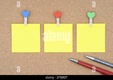 Three yellow stickers with multi-colored clothespins and ballpoint pens on a cork board. Stock Photo