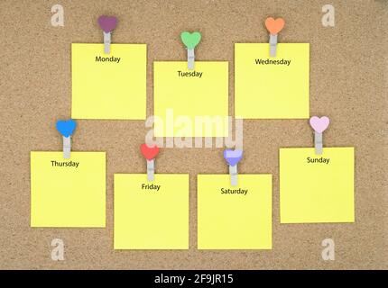 Seven yellow sticky notes with days of the week on a cork board. Stock Photo