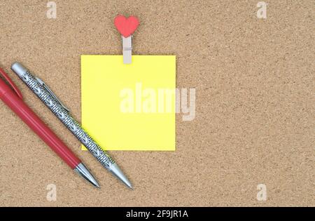 Yellow sticker with clothespin and ballpoint pens on a cork board. Stock Photo