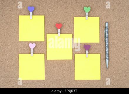 Six yellow stickers with multi-colored clothespins and ballpoint pen on a cork board. Stock Photo