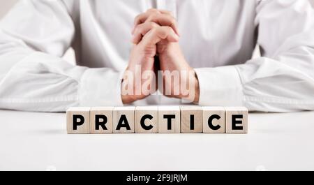 The word practice written on wooden cubes with a businessman with crossed hands at the background. Practice makes perfect concept. Stock Photo