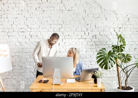 Young adult business partners working on new strategy for company, thinking about several ideas. Serious colleagues using computer, discussing Stock Photo
