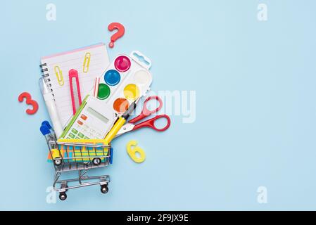 School supplies: pencils, pastels, rulers and notebook in a shopping cart, on blue background with copy space Stock Photo