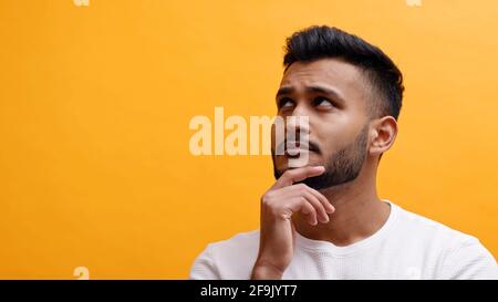 Portrait of handsome adult man touching his chin an looking up. Mixed race male model with modern quiff hair style against orange background. Stock Photo