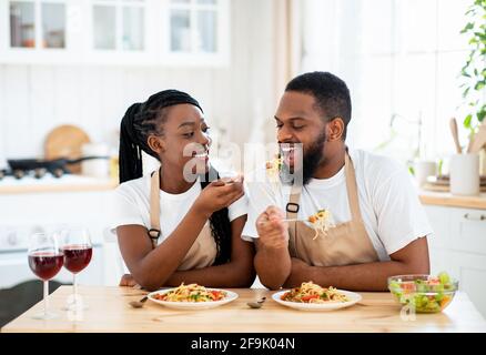 Happy Black Spouses Eating Lunch At Home, Enjoying Spaghetti And Wine Stock Photo