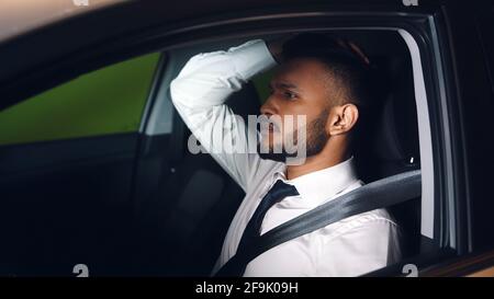 Businessman in white shirt sitting in car and holding his head. Stressed and worried mixed race man. Stock Photo