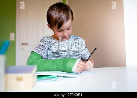 cool boy with green arm cast is sitting in his room and is writing something and is doing housework Stock Photo