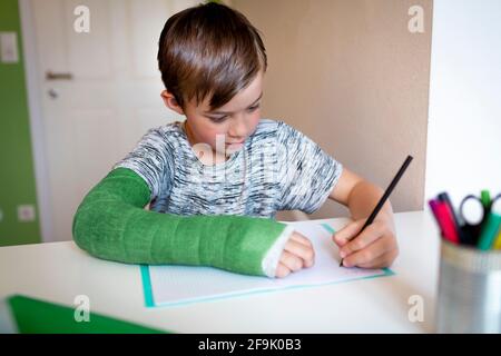 cool boy with green arm cast is sitting in his room and is writing something and is doing housework Stock Photo