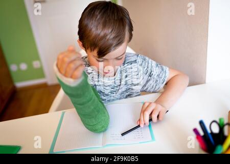 cool boy with green arm cast is sitting in his room and is writing something and is doing housework Stock Photo