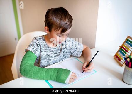 cool boy with green arm cast is sitting in his room and is writing something and is doing housework Stock Photo