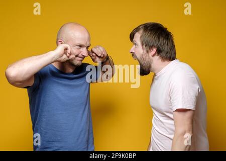 Two men, one in a rage screams loudly at the other who covered his ears with his fingers and looks calmly. Boss scolds the employee.  Stock Photo