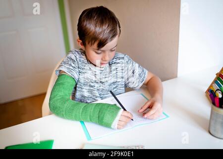 cool boy with green arm cast is sitting in his room and is writing something and is doing housework Stock Photo