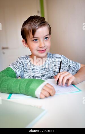 cool boy with green arm cast is sitting in his room and is writing something and is doing housework Stock Photo