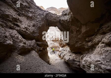Rider in green jacket at mountain bike in the desert Canyon cave in Kazakhstan. Extreme Sport and outdoor recreation concept. Stock Photo