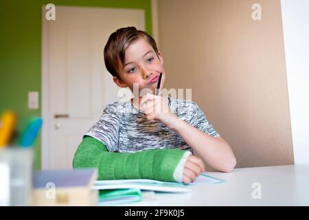 cool boy with green arm cast is sitting in his room and is writing something and is doing housework Stock Photo