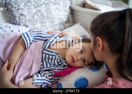 Mother looking after sick small daughter in bed at home, coronavirus concept. Stock Photo