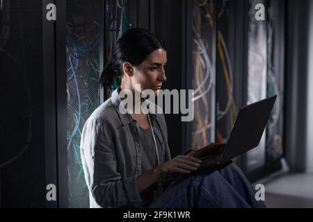 Side view portrait of female IT engineer using laptop in server room while working with supercomputer at data center, copy space Stock Photo