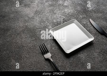 a white square empty plate, a black fork and knife. Stylish dinnerware for desserts. table setting. Suitable for interior decoration and design. copy Stock Photo