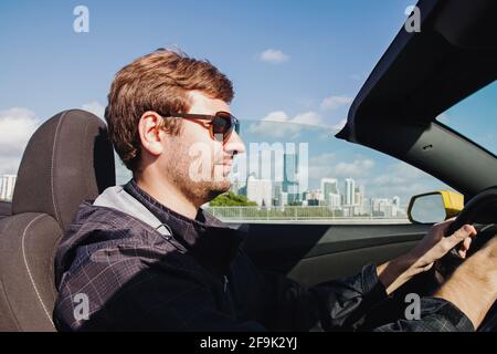 Man driving cabriolet car with a city skyline on the background Stock Photo